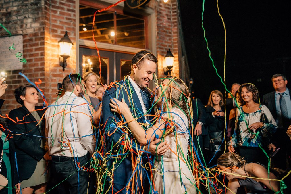bride and groom covered in colorful streamers during grand exit in front of butler's courtyard