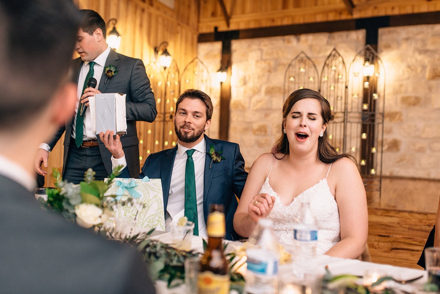 bride and groom laugh while best man gives a toast